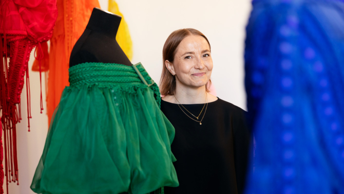 Sofia Ilmonen hymyilee kameralle. Ympärillä kaksi mallinukkea.